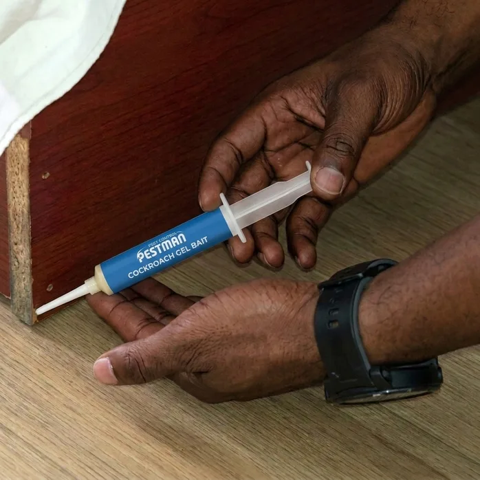 A hand laying a bead of Pestman gel into the seam at the base of a cabinet